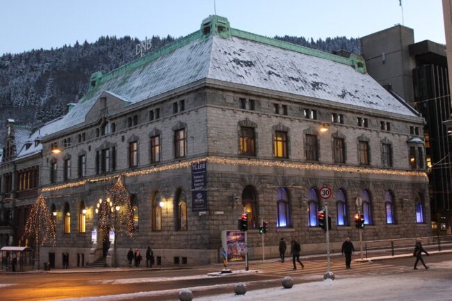 Granittbygget i Bergen med snø på taket og julelys langs fasaden.